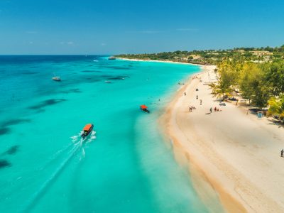Aerial view of boats on tropical sea coast with sandy beach at sunny day. Summer holiday on Indian Ocean, Zanzibar, Africa. Landscape with boat, palm trees, transparent blue water, hotels. Top view