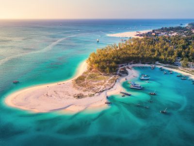 Aerial view of the fishing boats on tropical sea coast with sandy beach at sunset. Summer holiday on Indian Ocean, Zanzibar, Africa. Landscape with boat, green trees, transparent blue water. Top view